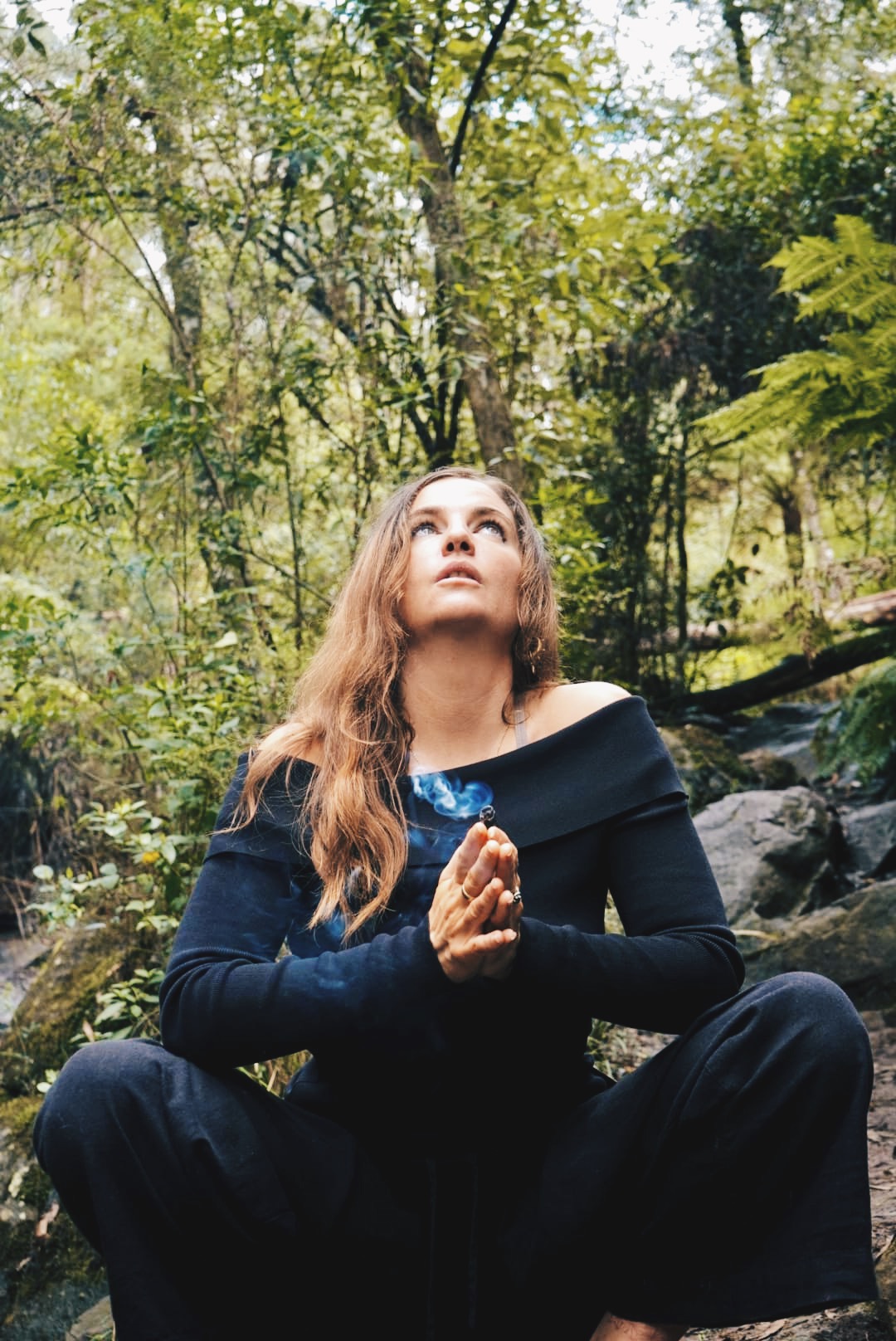 Portrait of Sarah Elizabeth seated cross-legged in a forest, hands in prayer with rising smoke